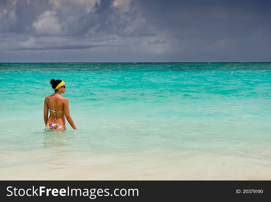 Tanned girls is standing in bright blue ocean under blue sky