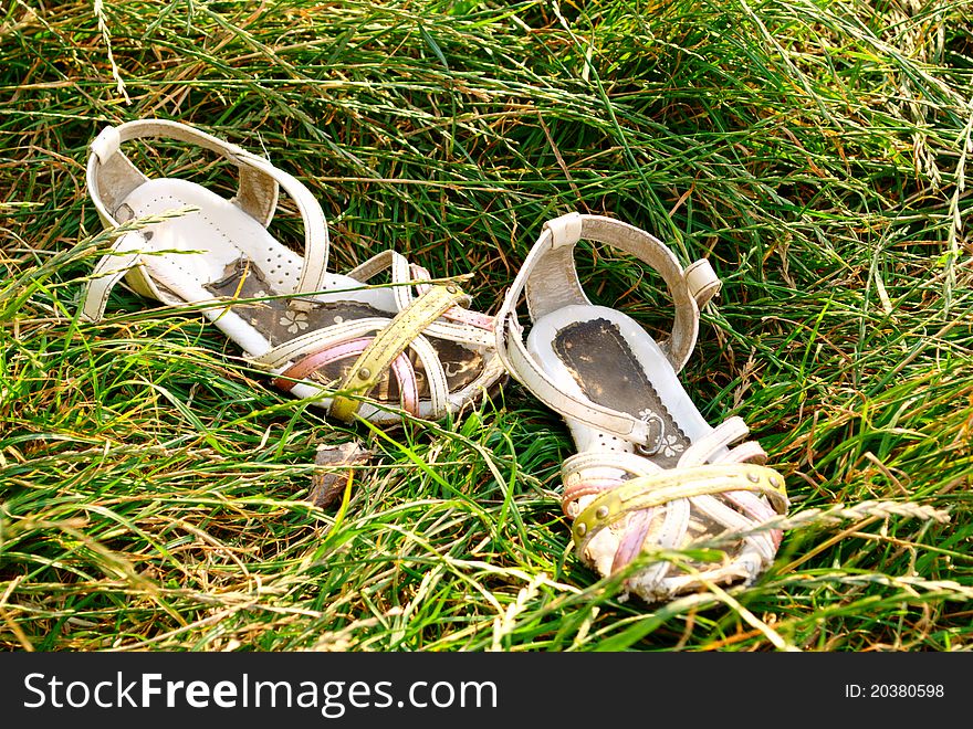 A couple of old children's shoes lay in the grass. A couple of old children's shoes lay in the grass