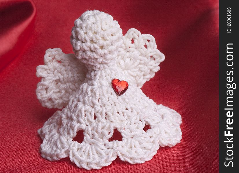 Handmade crochet Angel with a red heart on red satin background