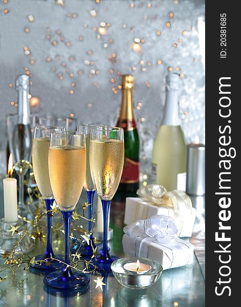 Champagne in glasses,bottles,gift boxes,candle lights and twinklelights on silver background. Champagne in glasses,bottles,gift boxes,candle lights and twinklelights on silver background.