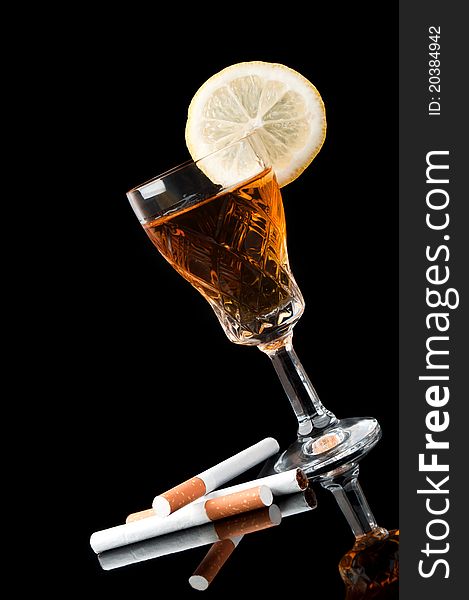 Cognac in a glass with lemon and cigarettes isolated on a black background