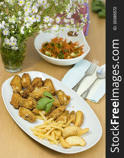 Golden fried chicken and fried potatoes in a white plate on the table