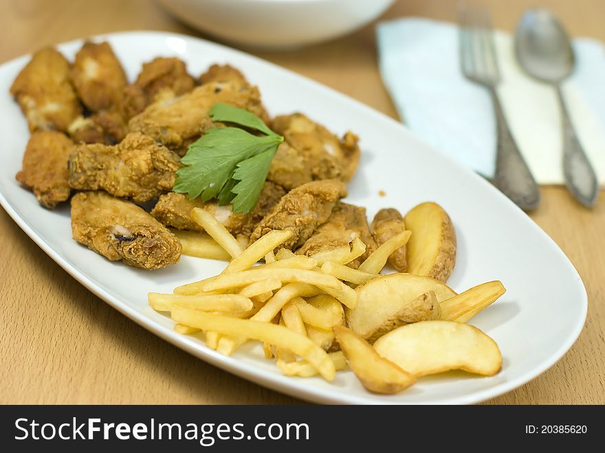 Golden fried chicken and fried potatoes in a white plate on the table