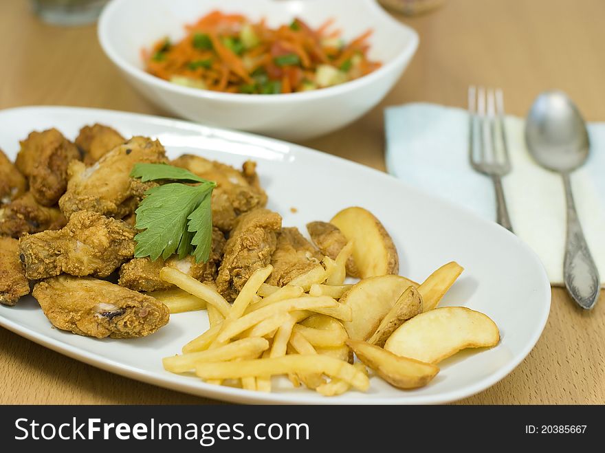 Golden fried chicken and fried potatoes in a white plate on the table