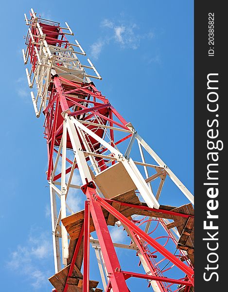Transmitting cellular tower. GSM transmitter. Communications tower. Red tower against the blue sky. Transmitting cellular tower. GSM transmitter. Communications tower. Red tower against the blue sky.