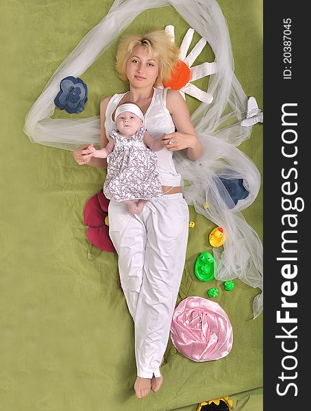 A young mother and her little daughter lie full-length on developmental mat. A young mother and her little daughter lie full-length on developmental mat