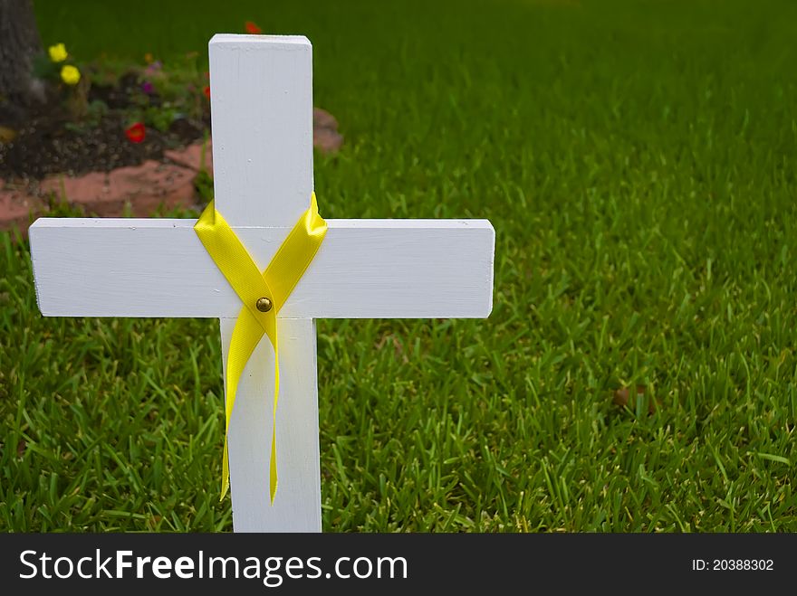 White cross with yellow ribbon seen against green grass and flower garden.