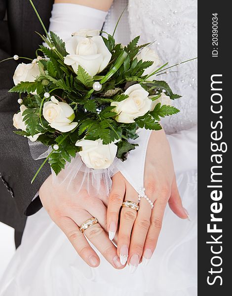 Hands of a newly-married couple with rings with a bouquet of the bride from white roses. Hands of a newly-married couple with rings with a bouquet of the bride from white roses