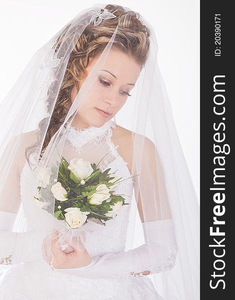 Studio portrait of a young bride wearing a white wedding dress with veil, holding flowers