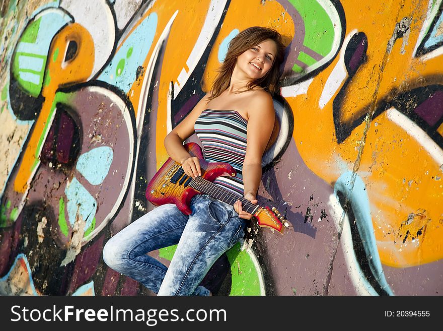 Beautiful brunette girl with guitar and graffiti wall at background.