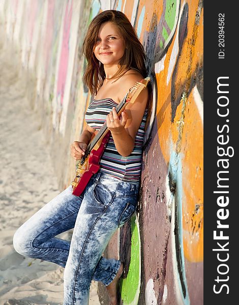 Beautiful brunette girl with guitar and graffiti wall at background.