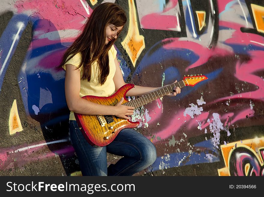 Beautiful brunette girl with guitar and graffiti wall at background.