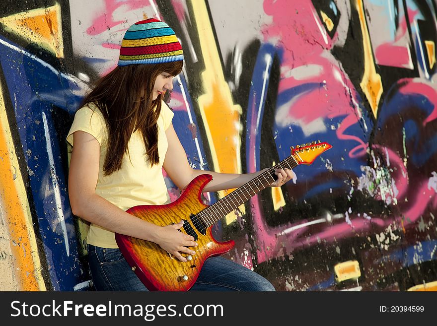 Beautiful brunette girl with guitar and graffiti wall at background.