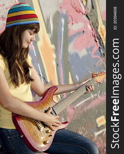 Beautiful brunette girl with guitar and graffiti wall at background.