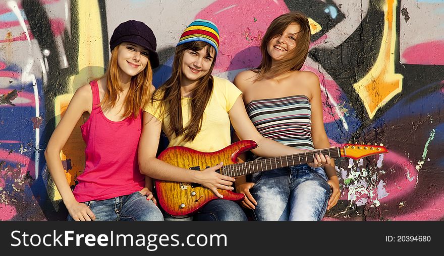 Three beautiful girls with guitar and graffiti wall at background.