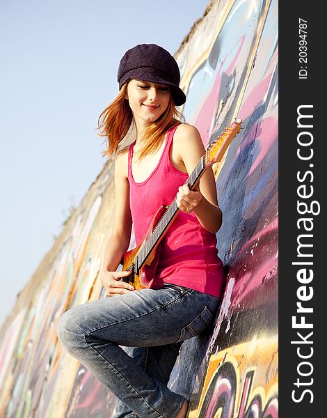 Beautiful red-haired girl with guitar and graffiti wall at background.