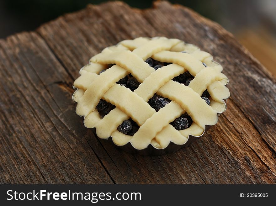 Unbaked fresh blueberry tartlet with lattice top on a wood. Unbaked fresh blueberry tartlet with lattice top on a wood