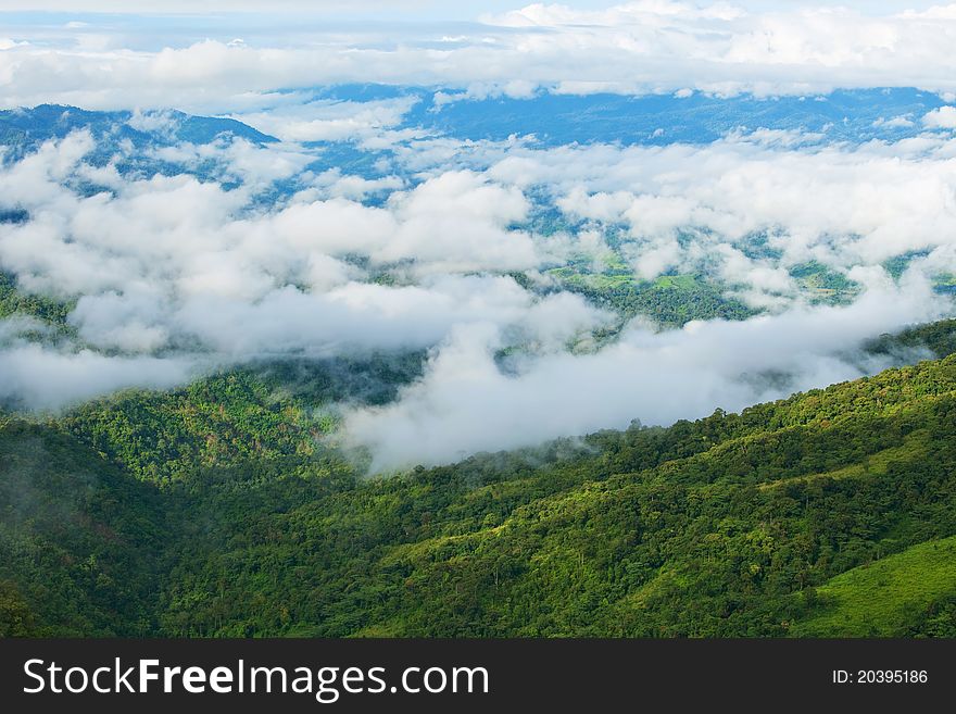 Mountain by green grass and cloudy blue sky