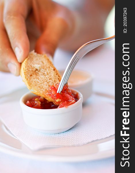 A picture of a red sauce in a small pot and a hand soping white bread into the sauce.