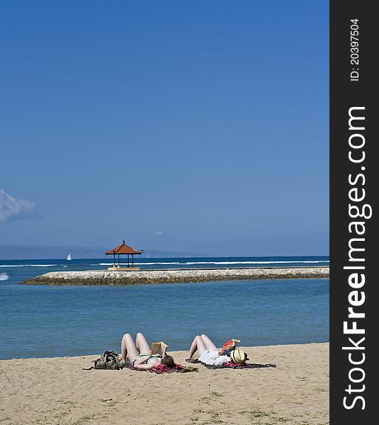 Two woman enjoy sunbathing and reading at the beach on their vacation