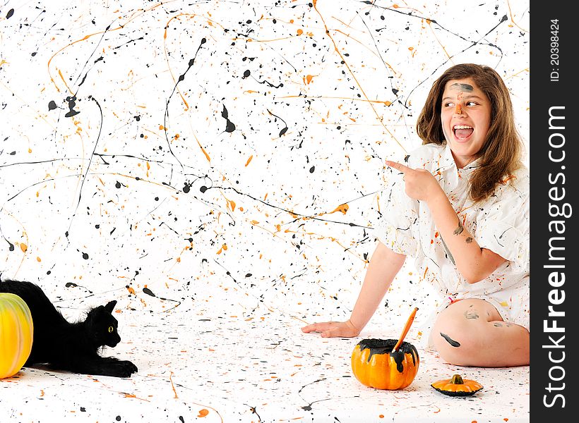 A preteen girl in a paint-splattered smock delightedly pointing to an area spashed with orange and black paint, otherwise left blank for your message. A black cat and pumpkin nearby. A preteen girl in a paint-splattered smock delightedly pointing to an area spashed with orange and black paint, otherwise left blank for your message. A black cat and pumpkin nearby.