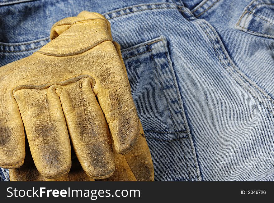 Worn pair of jeans, denim with thick pair of leather gloves stuck in backpocket. Worn pair of jeans, denim with thick pair of leather gloves stuck in backpocket