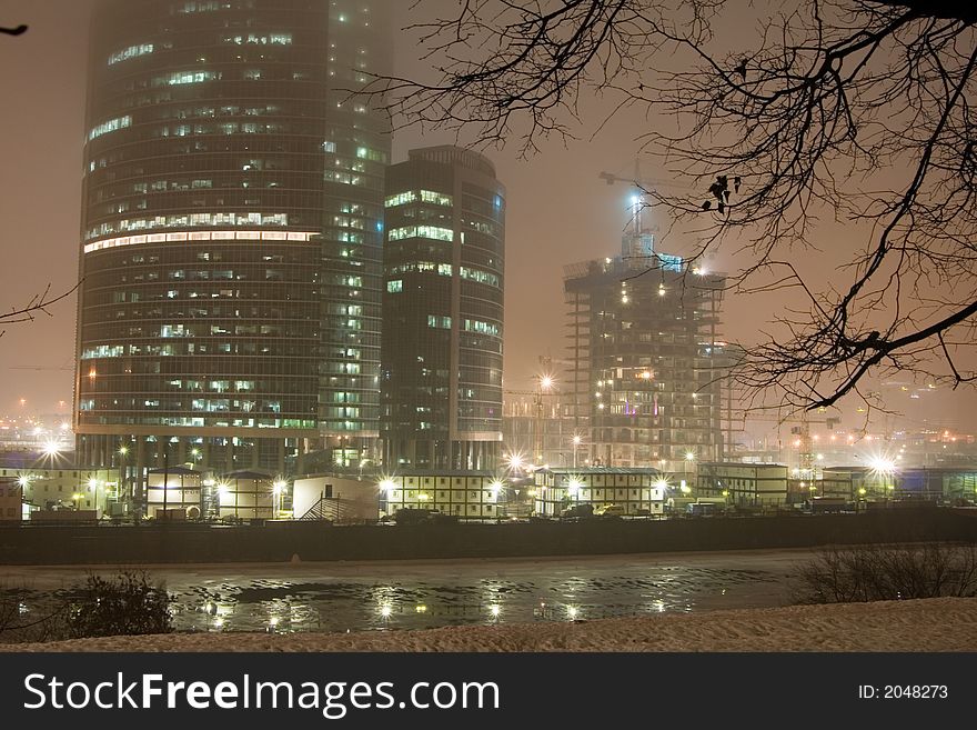 Highrise buildings, river and fog at night city.