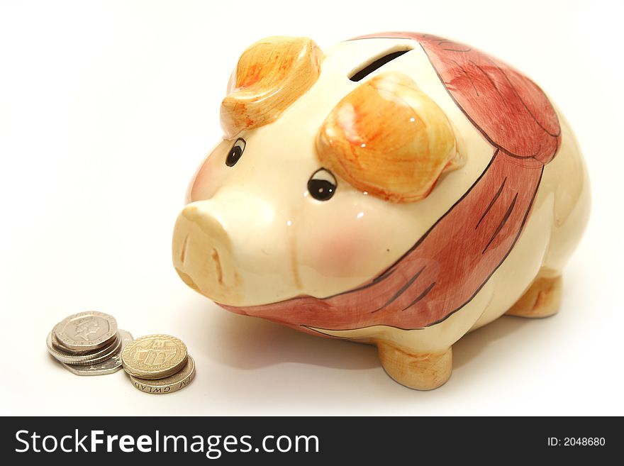 A cute, porcelain piggy bank next to stirling pound coins, isolated on a white background. A cute, porcelain piggy bank next to stirling pound coins, isolated on a white background.