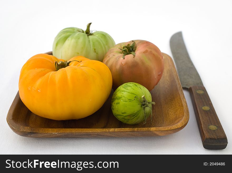 Varieties of organic heirloom tomatoes on a wooden plate with a huge knife. Farm fresh produce. Varieties of organic heirloom tomatoes on a wooden plate with a huge knife. Farm fresh produce.