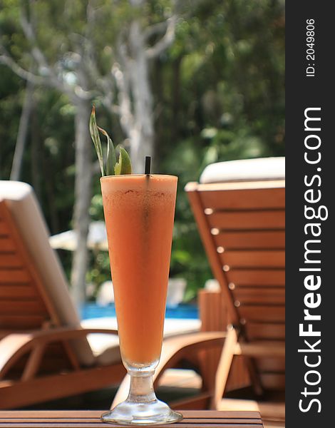 Fruit juice at a resort with deck chairs and pool in back ground