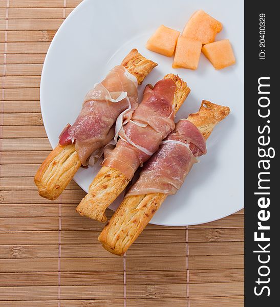 Prosciutto on grissini and melon on the plate