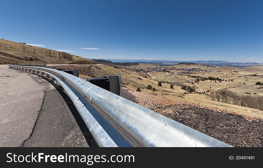 A wide angle shot of a curving road overlooking Cripple Creek, Colorado with snow capped mountains in the distance.