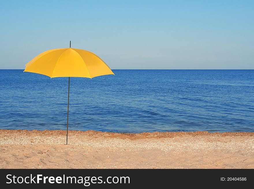 Yellow parasol, standing on the shore of the evening sea