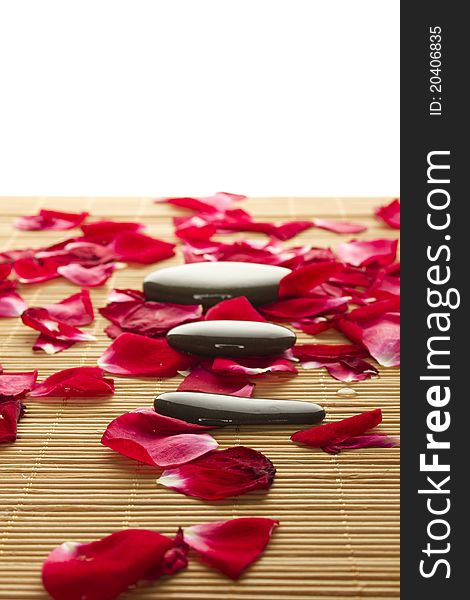 Close-up of three polished stones lie strewn on a wooden surface with rose petals. Close-up of three polished stones lie strewn on a wooden surface with rose petals