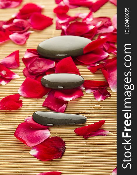 Close-up of three polished stones lie strewn on a wooden surface with rose petals. Close-up of three polished stones lie strewn on a wooden surface with rose petals