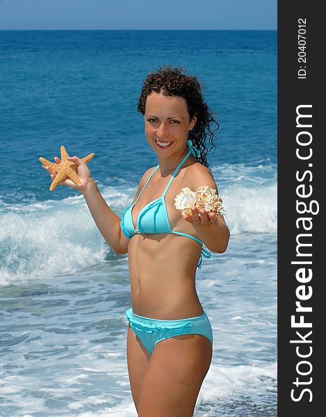 The happy young woman with cockleshell and starfish on a beach