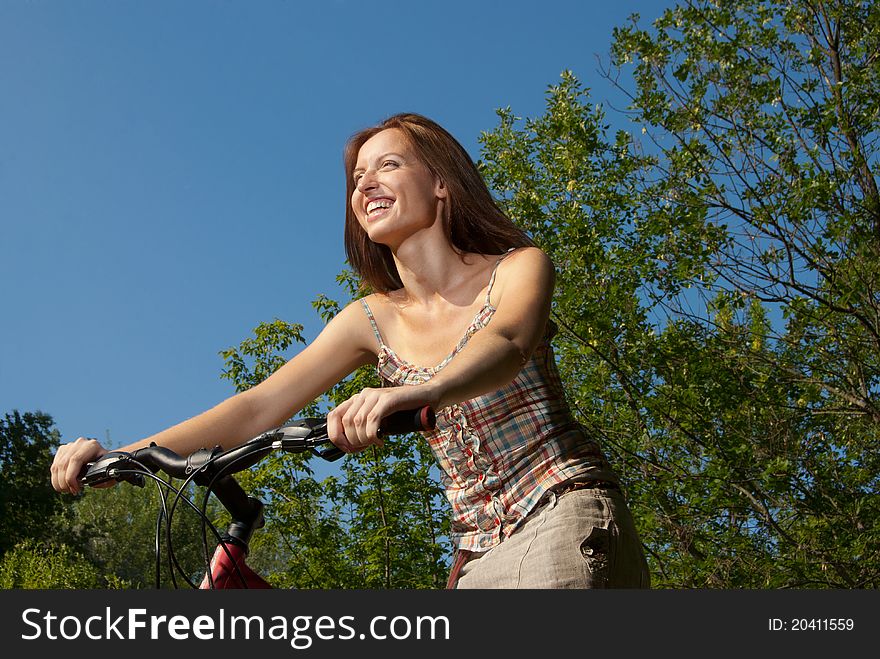 Portrait of pretty young woman with bicycle in a park smiling - Outdoor
