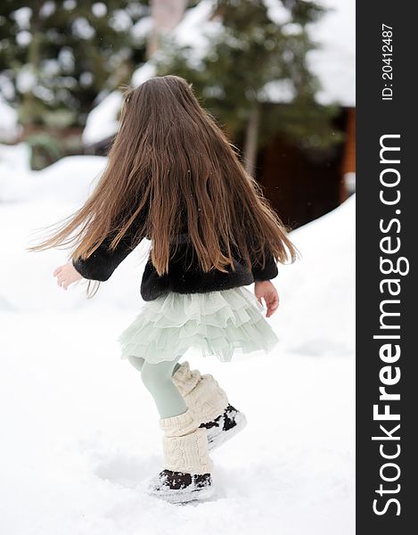 Long-haired brunette girl in tutu skirt, fur jacket and legwarmers dances in the snow. Long-haired brunette girl in tutu skirt, fur jacket and legwarmers dances in the snow