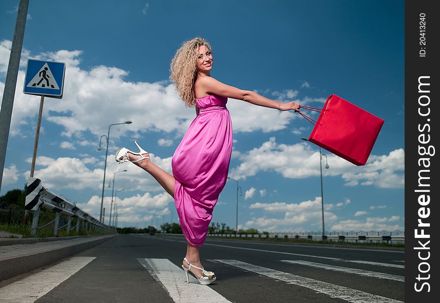 Woman in a pink dress with a bag goes over the road