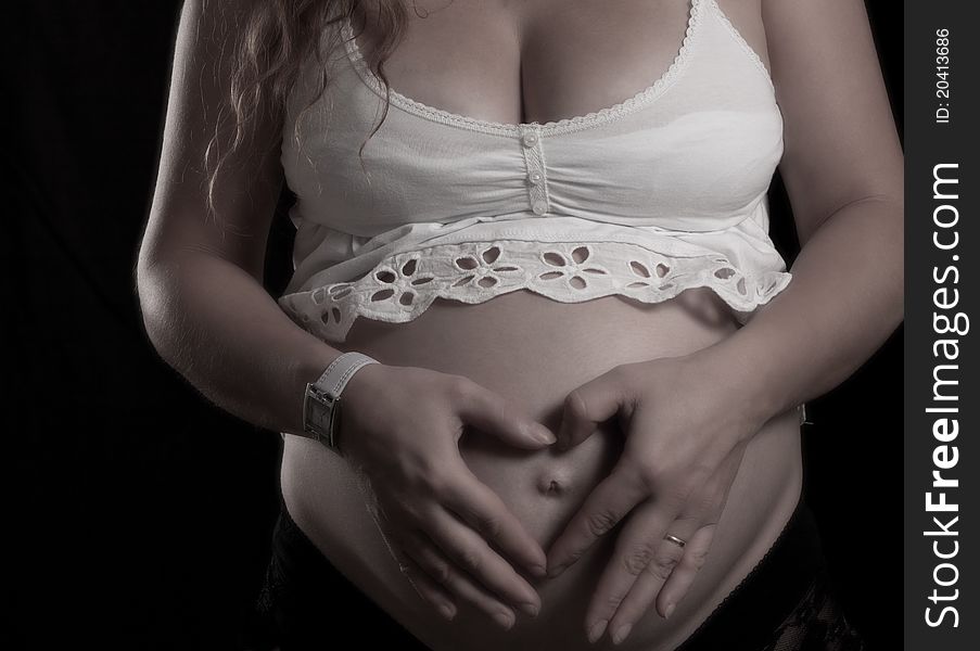 Heart shape hands on a pregnant women belly on black background. Heart shape hands on a pregnant women belly on black background