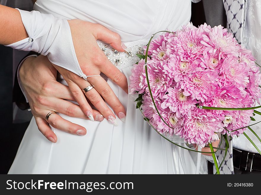 Bride and groom hands with wedding rings and bouquet of chrysanthemums