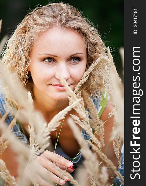 A beautiful blond haired blue eyed model wearing a sits amid tall grass