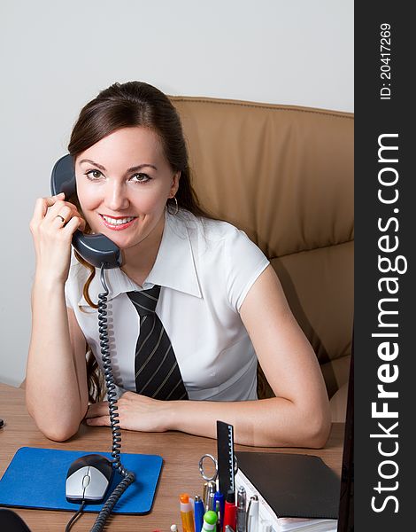 Beautiful business woman in a tie and white shirt with long hair holding the phone at the desk in the office. Beautiful business woman in a tie and white shirt with long hair holding the phone at the desk in the office