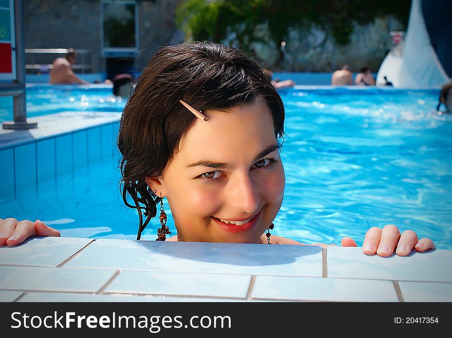 Close up portrait of a beautiful happy woman resting on her hands at the side of a sun bathed swimming pool