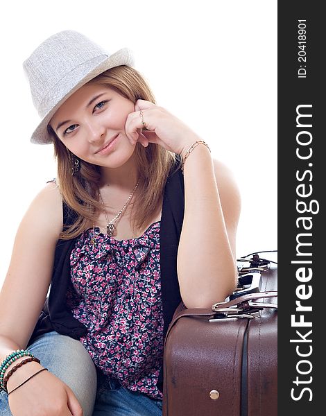 Attractive girl in hat is sitting near vintage suitcase. Studio shot isolated over white background