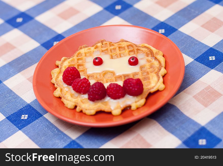 Handmade smiling cookie with raspberries on a checkered tablecloth