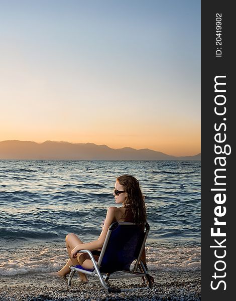 Beautiful young woman sitting on chair on beach and watching sunset. Beautiful young woman sitting on chair on beach and watching sunset