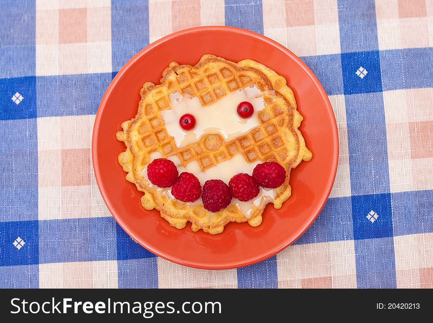 Handmade smiling cookie with raspberries on a checkered tablecloth