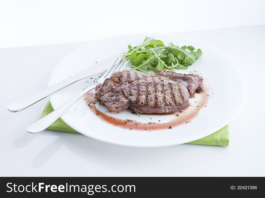 Grilled beef, served with arugula on a plate, view of the table with a white background