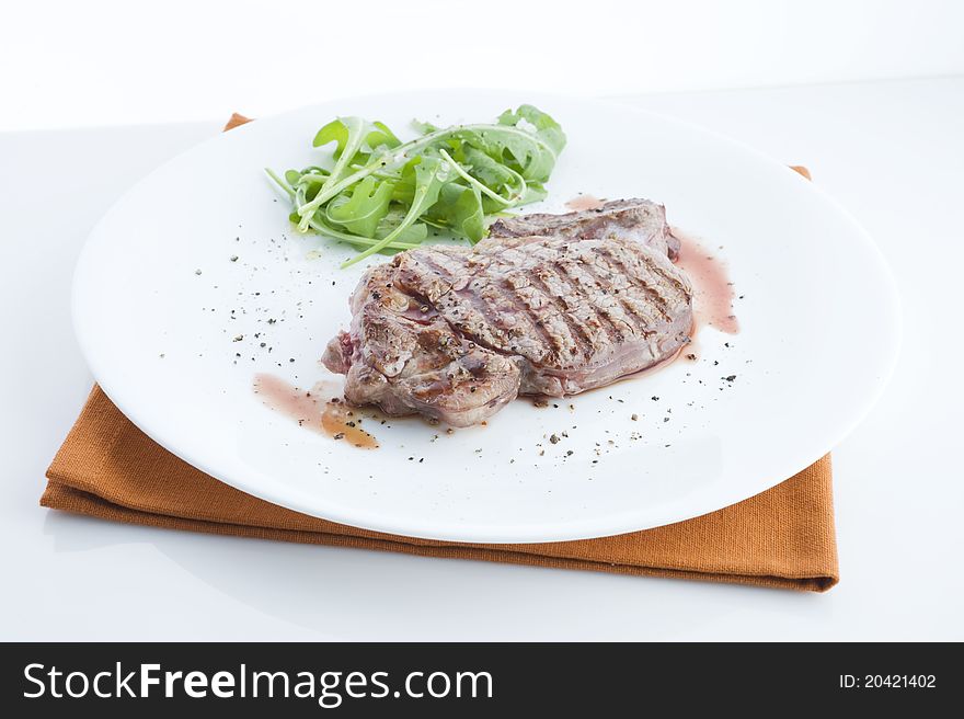 Grilled beef, served with arugula on a plate, view of the table with a white background